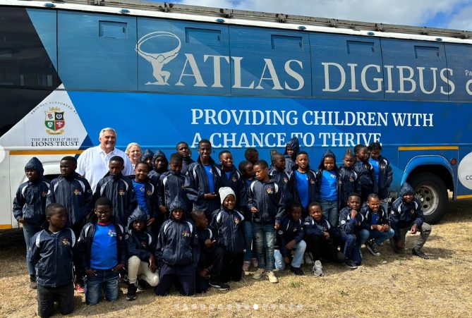 A large group of learners and staff gathered in front of the Atlas DigiBus